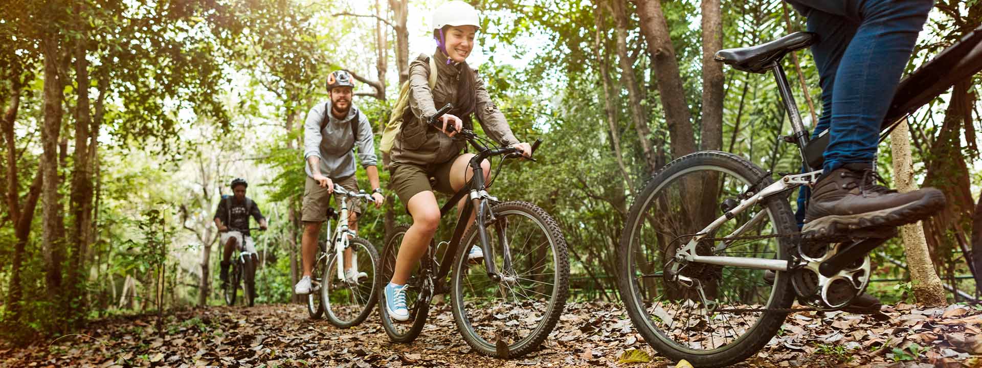 Three club members riding mountain bikes along a sunlit forest trail.