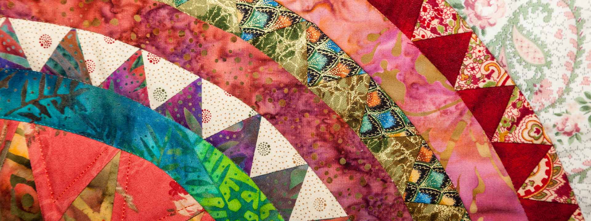 A close-up of a brightly colored patchwork quilt pieced from curved batik fabrics.