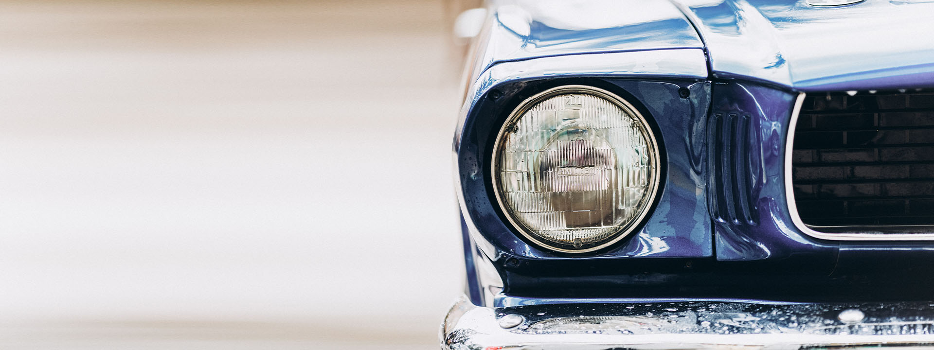 A tight crop of the round chrome headlight on the front of a deep blue classic car.