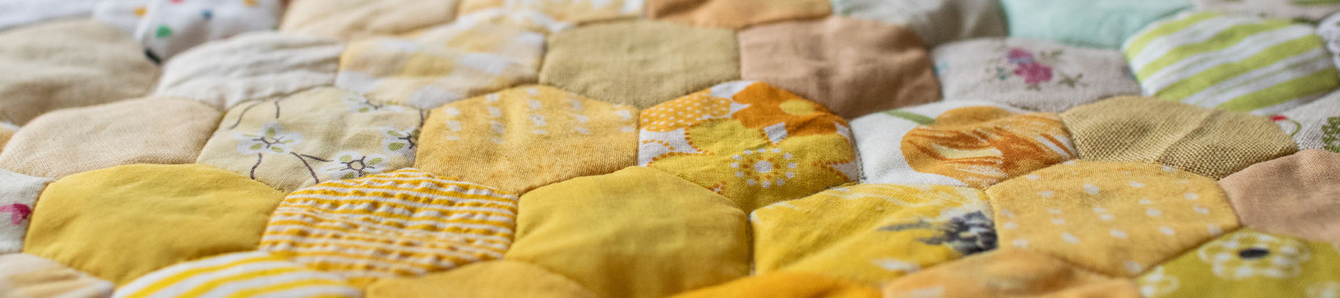 A short banner crop of a vintage quilt pieced from yellow hexagon patches in many patterns.