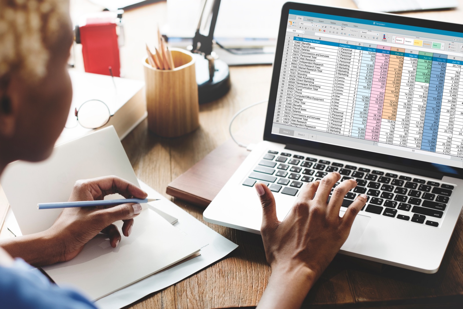 Reviewing a colorful multi-tab spreadsheet on a laptop at a home-office desk.