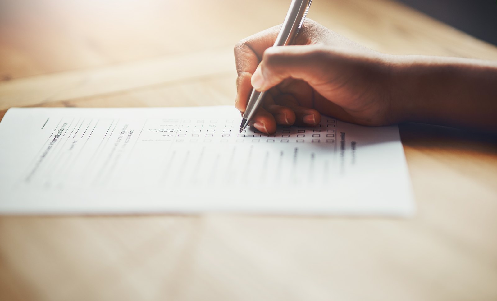 A hand filling in a paper survey form with tick-box rating scales, on a wooden table.