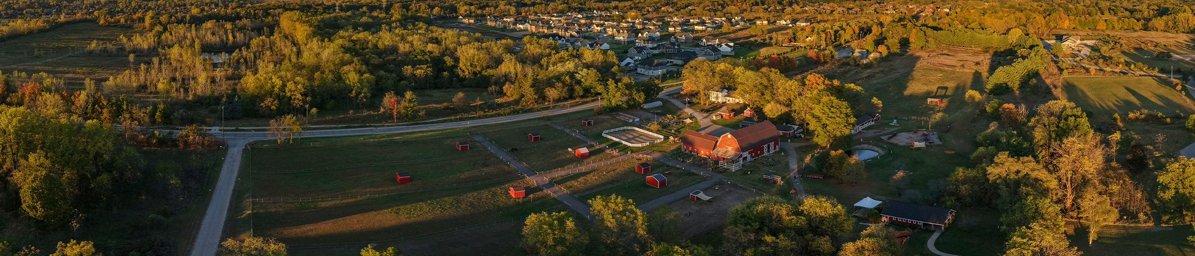 Aerial view of a historic farmstead with a red barn at sunset, a small town beyond, representing the town, county, and heritage societies that run on Clubistry.